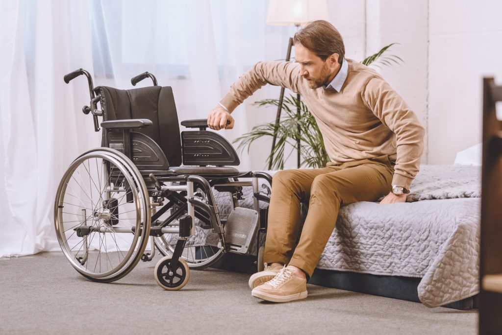 man with disability trying to sit on wheelchair from bed